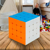 A 4x4 speed cube with blue, orange, and white sides sits on a wooden table in a child's room.