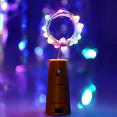 A brown bottle cork with a string of colorful LED lights coiled into a circle, glowing brightly against a purple background.