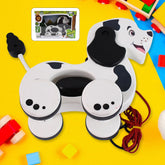 A white and black spotted dog pull toy with a red string on a yellow and blue surface, with its retail box in the upper left