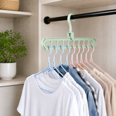 Light green multi-hole hanger holding various shirts on blue and pink hangers inside a closet.