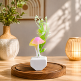 A mushroom night light with pink and yellow caps and green leaves sits on a wooden tray with a vase and lantern in the