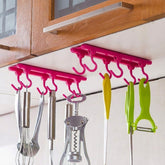 Two pink plastic hanging racks with six hooks each, holding kitchen utensils under a wooden cabinet.