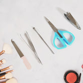Five silver manicure tools with blue and pink handles are spread out on a white surface next to makeup brushes.