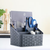A gray woven-look plastic desk organizer with five compartments holds various office supplies like pens, scissors, and a