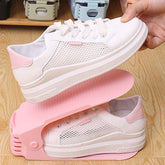 A hand places a white and pink sneaker onto a pink plastic shoe organizer, with another shoe already on a lower level.
