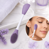 Purple and white double-headed silicone brush with a textured end and a spatula end, near a white towel and lavender flowers.