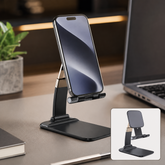Black and gold foldable phone stand holding a smartphone on a desk next to a laptop and plant.