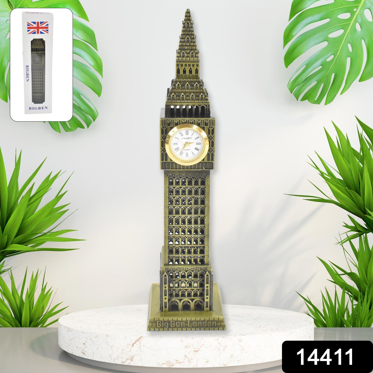 A tall, bronze-colored Big Ben clock tower replica with a white clock face stands on a white pedestal, surrounded by green