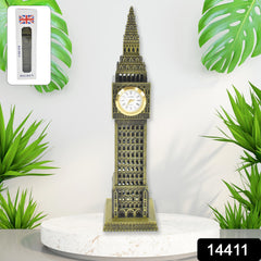 A tall, bronze-colored Big Ben clock tower replica with a white clock face stands on a white pedestal, surrounded by green