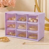 A light purple nine-compartment organizer filled with various gold and pearl jewelry items on a marble surface.