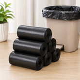 Six rolls of black garbage bags stacked next to a white trash can with a bag inside.