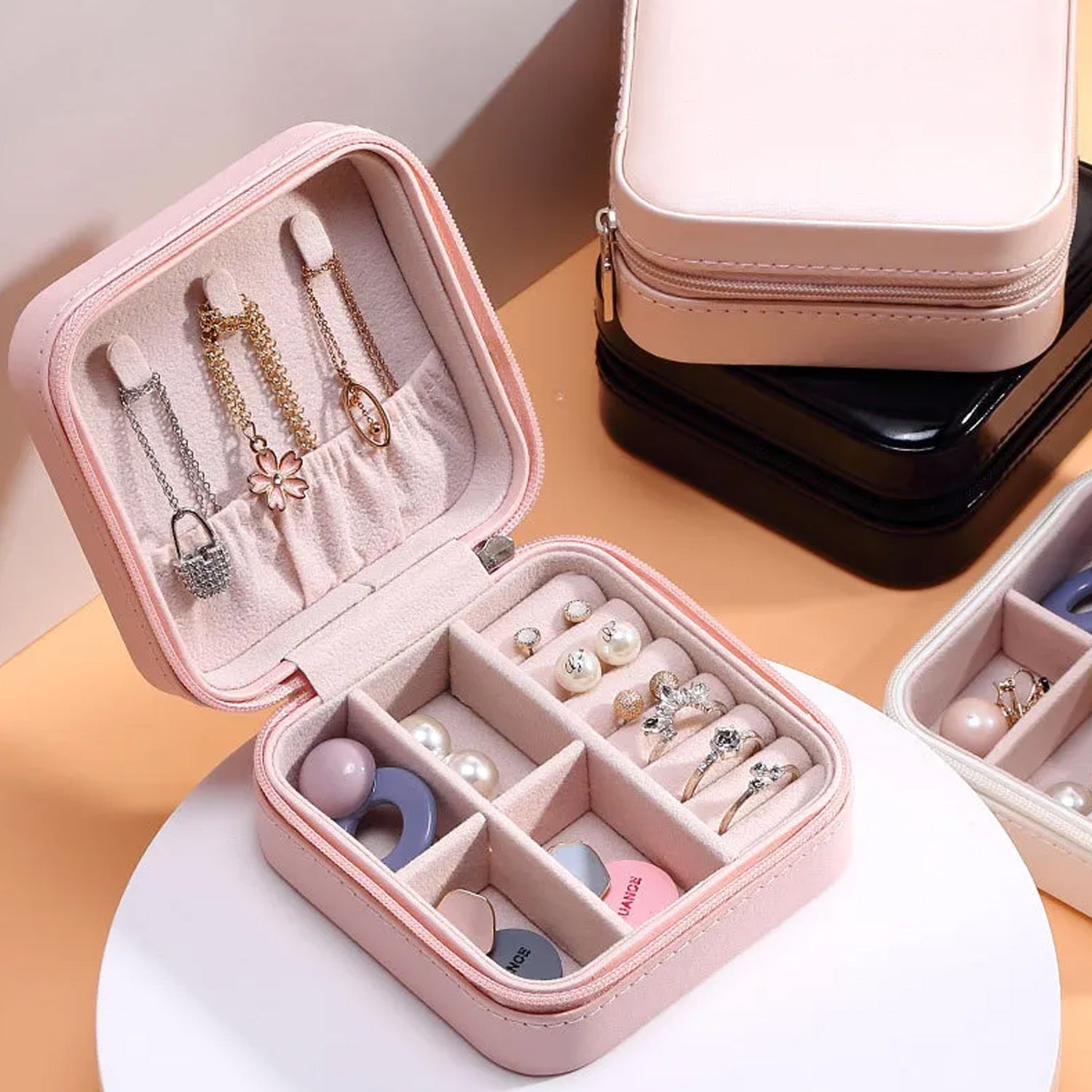 Open pink jewelry box with various pieces of jewelry, next to closed black and white boxes.