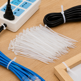 A pile of white cable ties on a wooden surface, with a power strip, black cable, and blue cable also secured with ties.