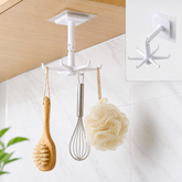 A white 360-degree rotating hook with six prongs hangs from a wooden cabinet, holding a wooden brush, whisk, and loofah.