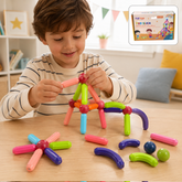 A young boy plays with colorful magnetic sticks and balls, building a small structure on a wooden table.