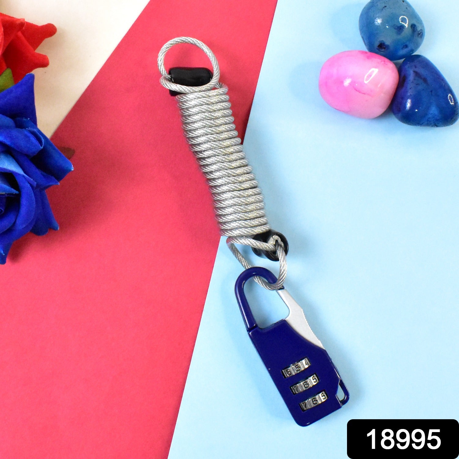 A blue carabiner-style combination lock with a silver coiled wire attached, displayed on a pink and blue surface.