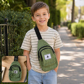 A young boy smiles, wearing a light green canvas sling bag with a front pocket and black strap. The bag has a white label