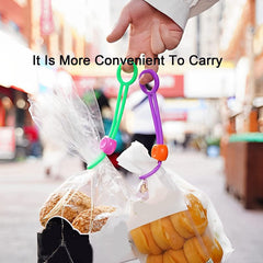 A hand holds two plastic bags, secured with a green and a purple silicone bag clip, while walking outdoors.