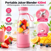Pink portable juicer blender filled with fruit, surrounded by cut mango, strawberries, and blueberries.