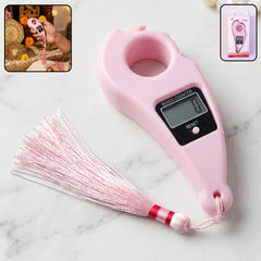A person's hand holds a pink digital finger counter with a tassel, positioned above a traditional prayer setup with brass