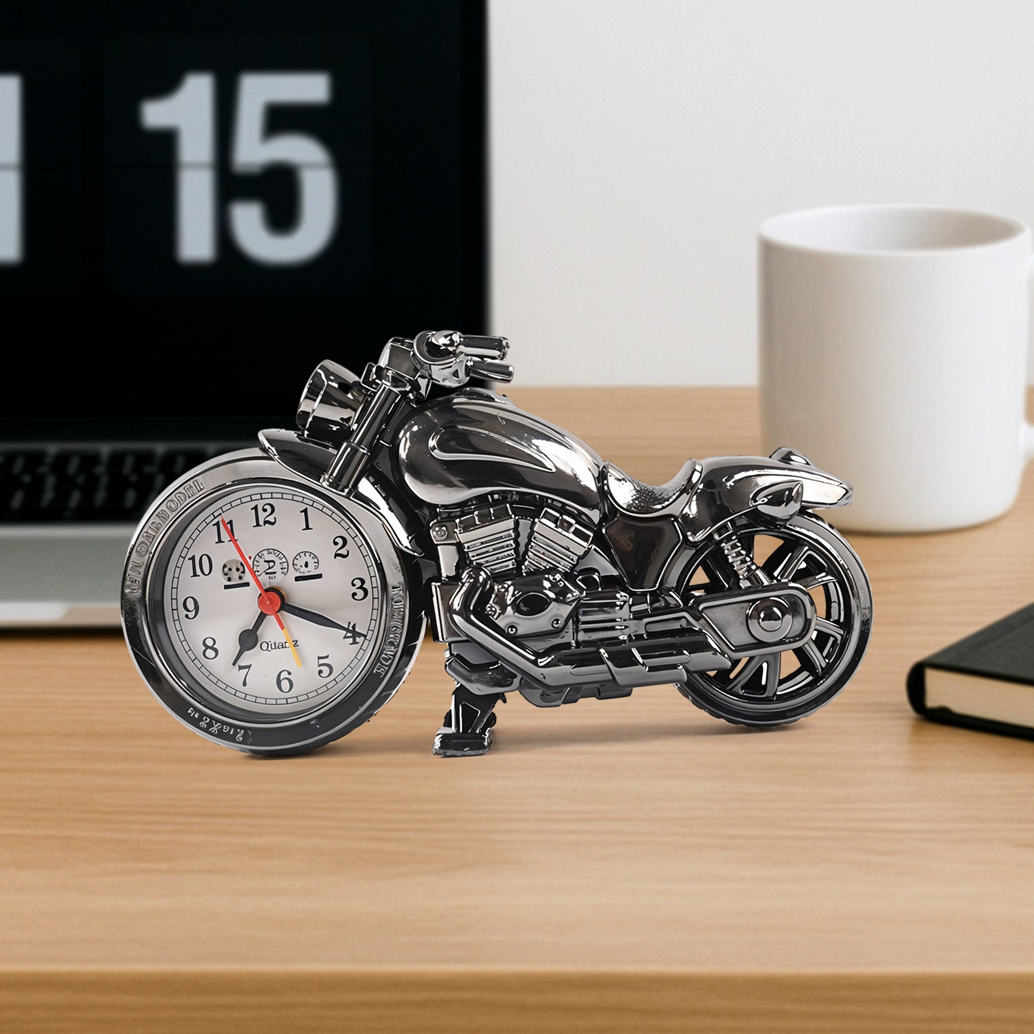 A shiny silver motorcycle clock sits on a wooden desk next to a laptop and white mug.