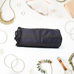 The upright black drawstring pouch is displayed on a light pink surface with makeup items and yellow flowers.