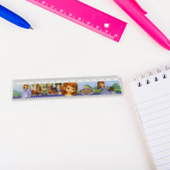 A Sofia the First ruler lies on a white desk next to a spiral-bound notebook and a blue pen.