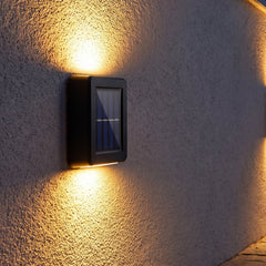 Two black solar wall lights illuminating a dark grey exterior wall with warm, bright beams.