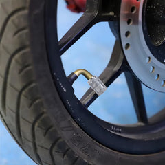 A silver metal valve cap with a textured grip is screwed onto a tire valve stem on a vehicle wheel.