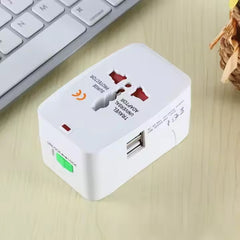 A white universal travel adapter with red outlets and two USB ports rests on a wooden surface next to a keyboard.