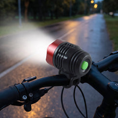 A red and black bicycle headlight with a green button lights up a dark road from a handlebar perspective.