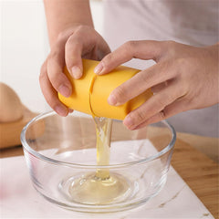 A person's hands are shown using a yellow egg cracker tool to separate egg whites from a yolk into a clear glass bowl. The