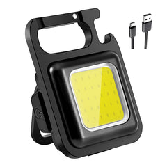 A black rectangular mini flashlight with a carabiner clip and bottle opener, showing its yellow LED panel and two charging
