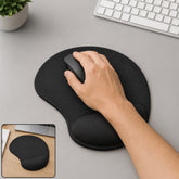 A hand using a mouse on a black ergonomic mouse pad with wrist support, next to a keyboard and plant.