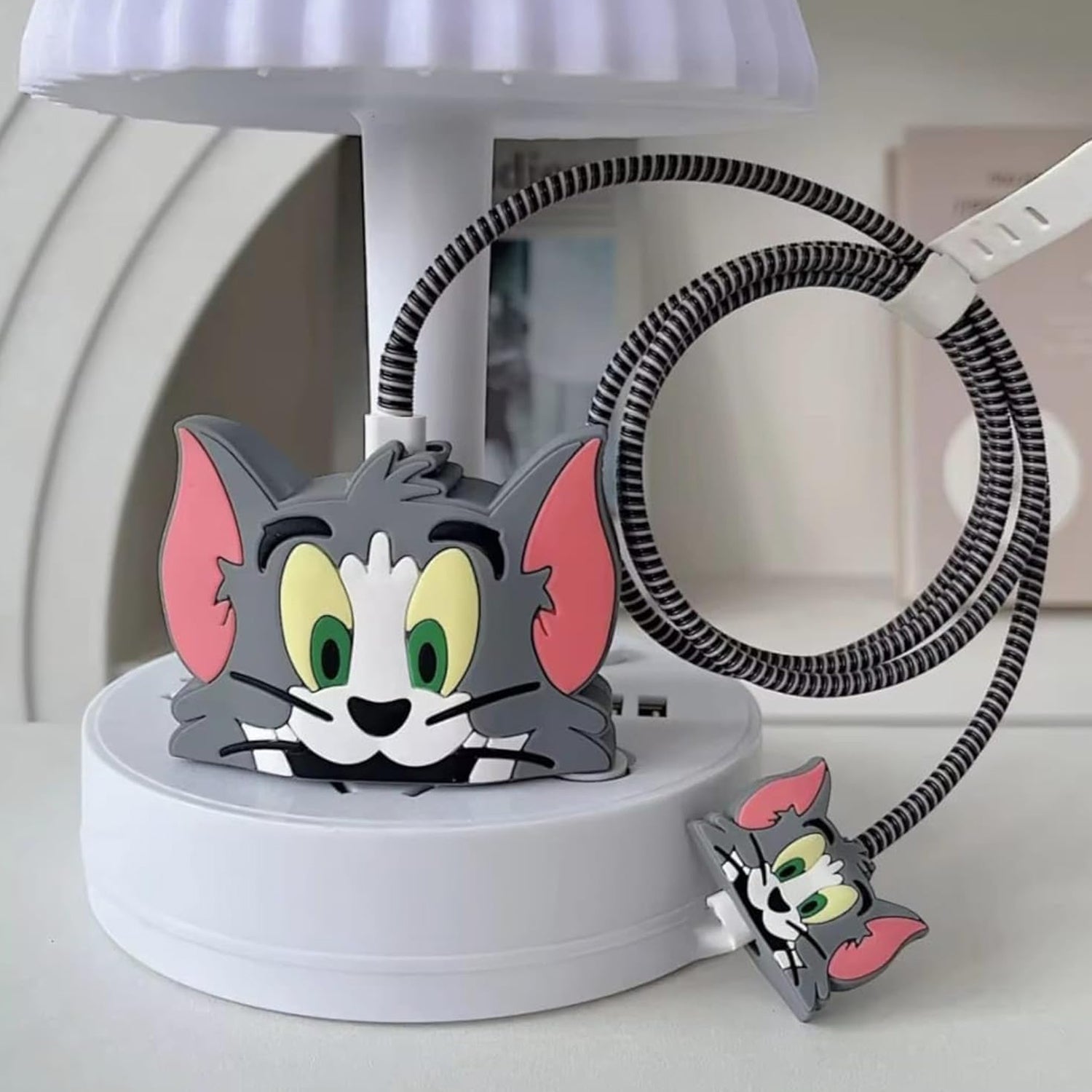 Gray Tom cat silicone charger cover with a striped cable protector on a white lamp base.