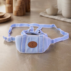 A light blue baby walking harness with white stripes and a brown emblem, displayed on a light brown surface with colorful