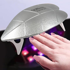 A silver leaf-shaped UV LED nail lamp cures light pink polished nails with purple light.