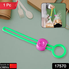 A vibrant green silicone bag clip with a pink button closure, featuring a ring on one end, displayed on a grey surface. The