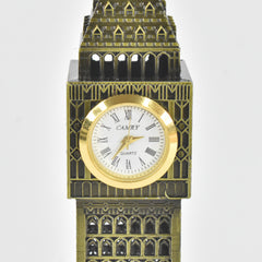 The bronze Big Ben clock tower replica lies horizontally on a two-toned pastel surface, adorned with delicate pink and green