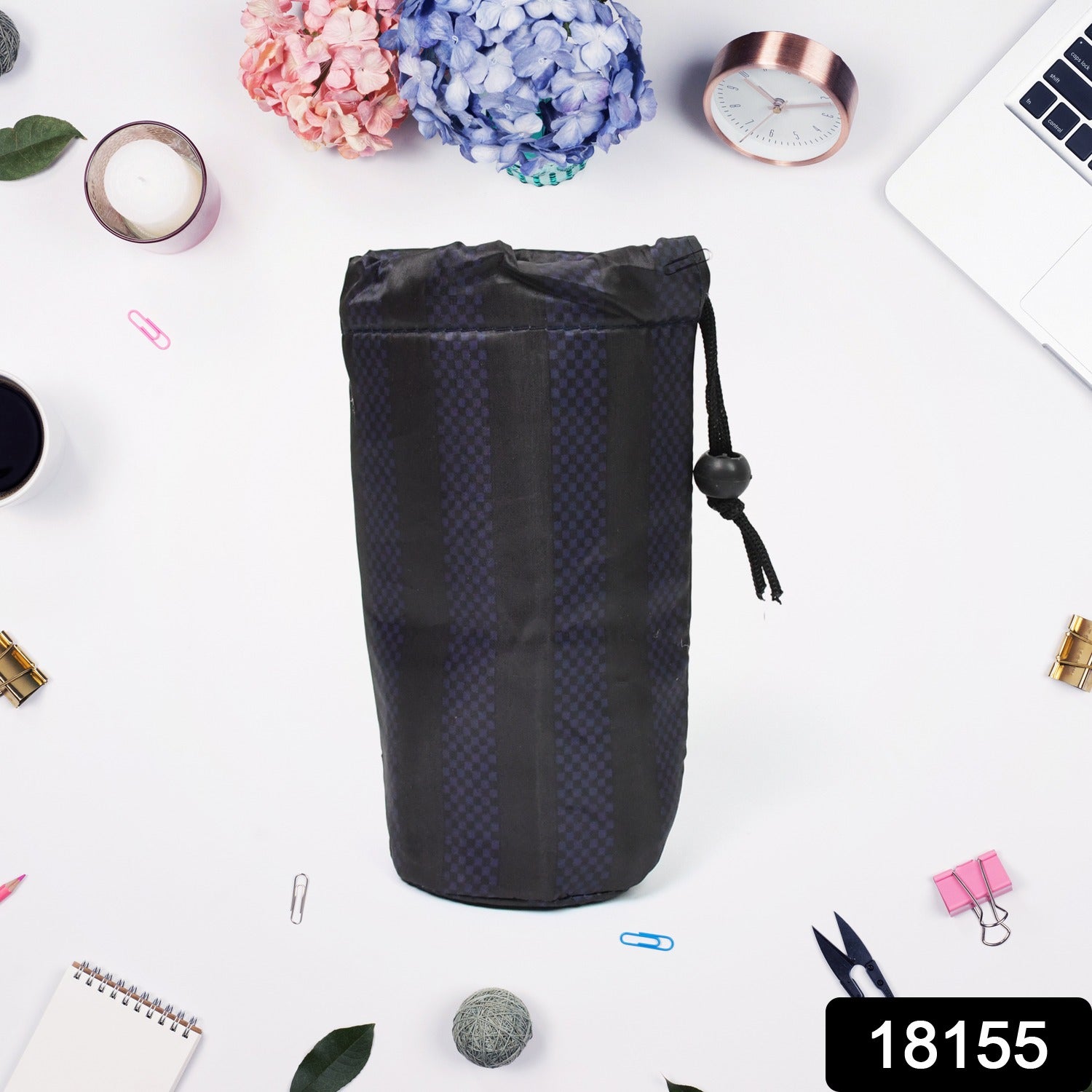A black drawstring pouch with a subtle checkered stripe pattern stands upright on a white desk with office supplies.
