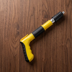 A yellow and black manual nail gun tool rests diagonally on a warm brown wooden surface.
