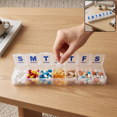 A hand places a white pill into a clear plastic pill organizer filled with various colorful medications on a wooden – view 2