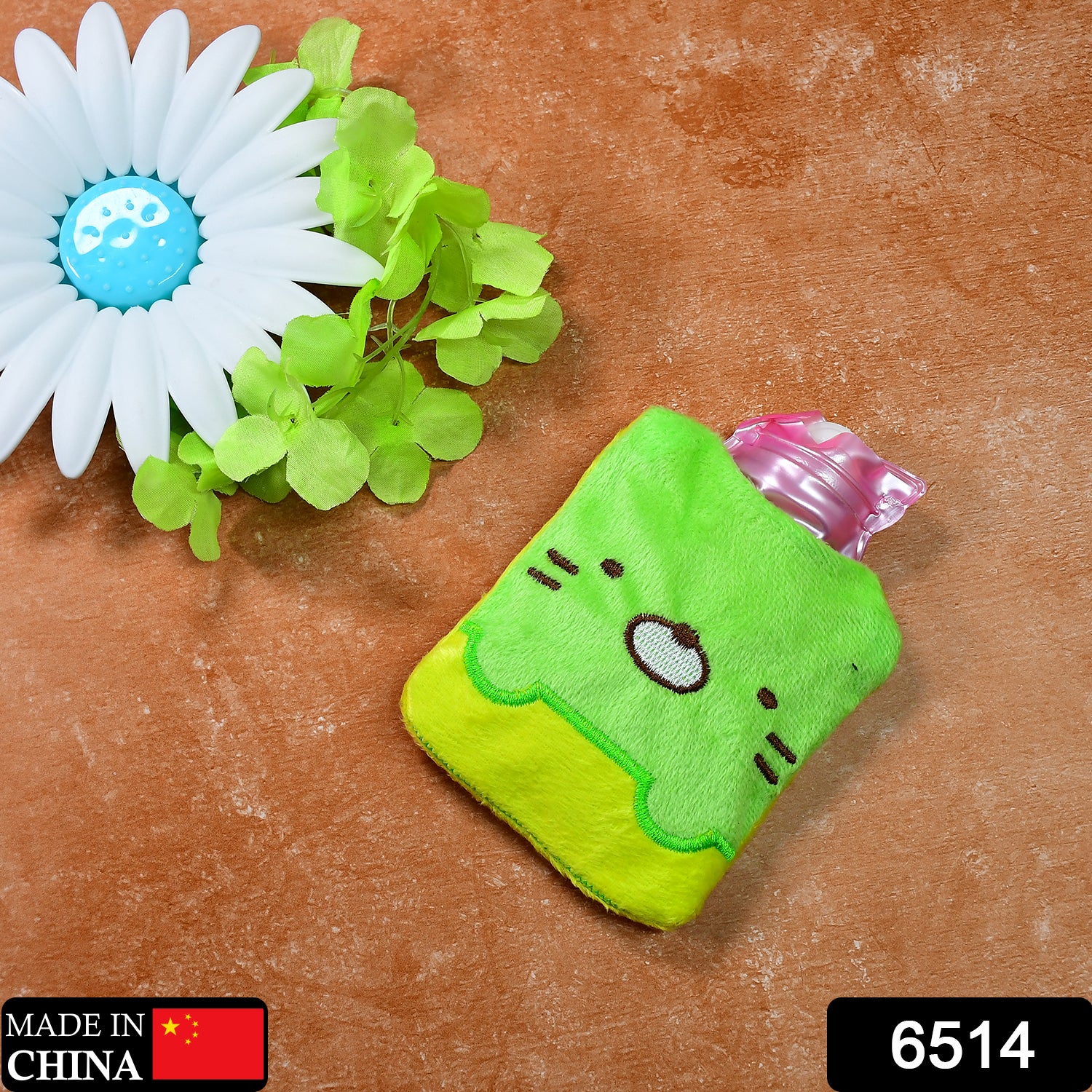 A green and yellow kitty hot water bag with a pink bottle, next to a white flower.