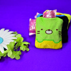 A green and yellow kitty hot water bag with a pink bottle, on a purple surface.