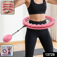 A woman in black activewear uses a pink weighted hula hoop with an attached oval massage ball.
