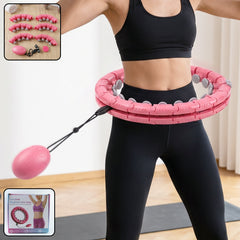 A woman exercises with a pink weighted hula hoop, featuring a small oval massage ball attached by a string.