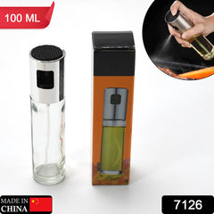 A clear glass and silver oil sprayer next to its orange and black packaging, with a small inset of it spraying.