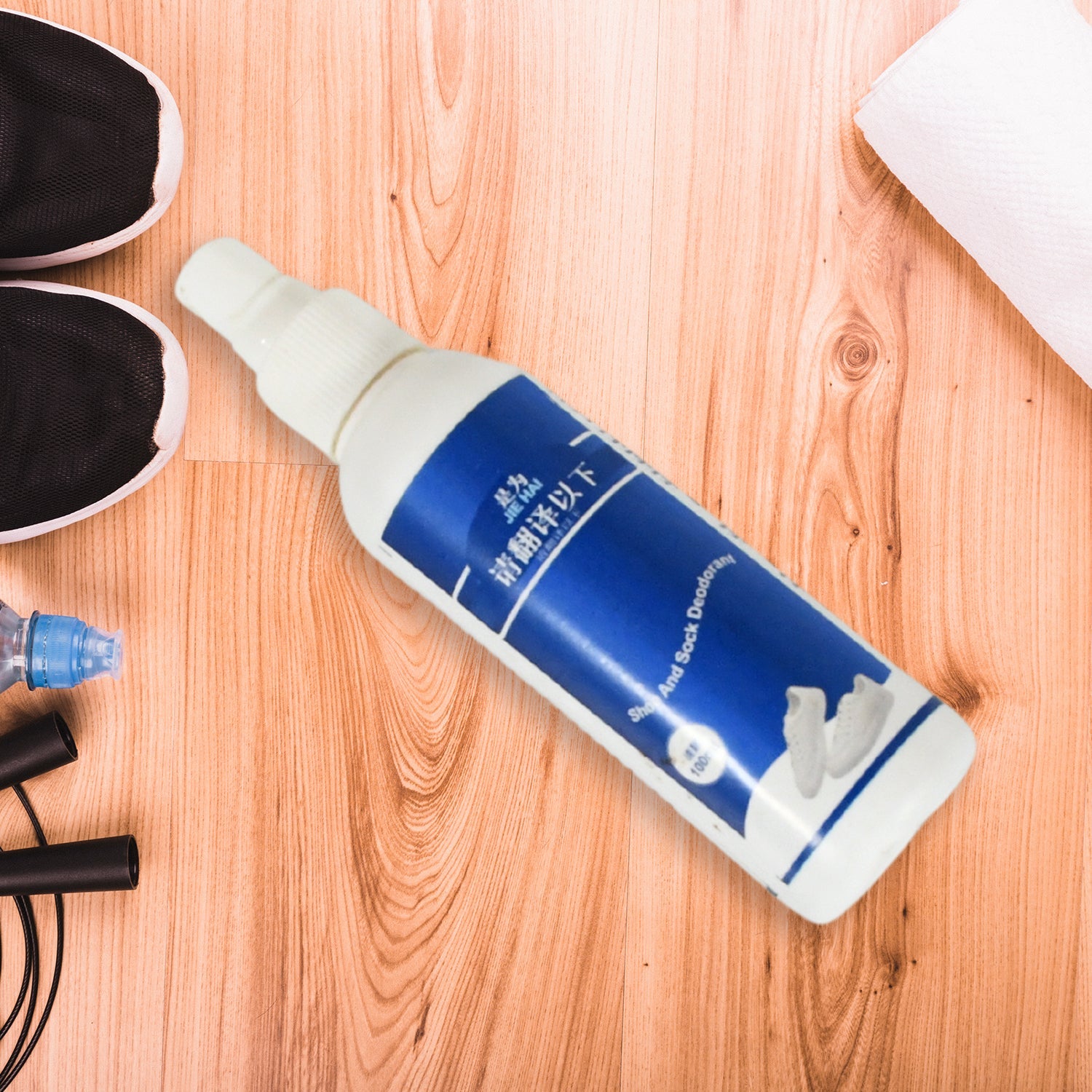A white and blue bottle of shoe and sock deodorant lies on a light wooden surface next to black athletic shoes, a white