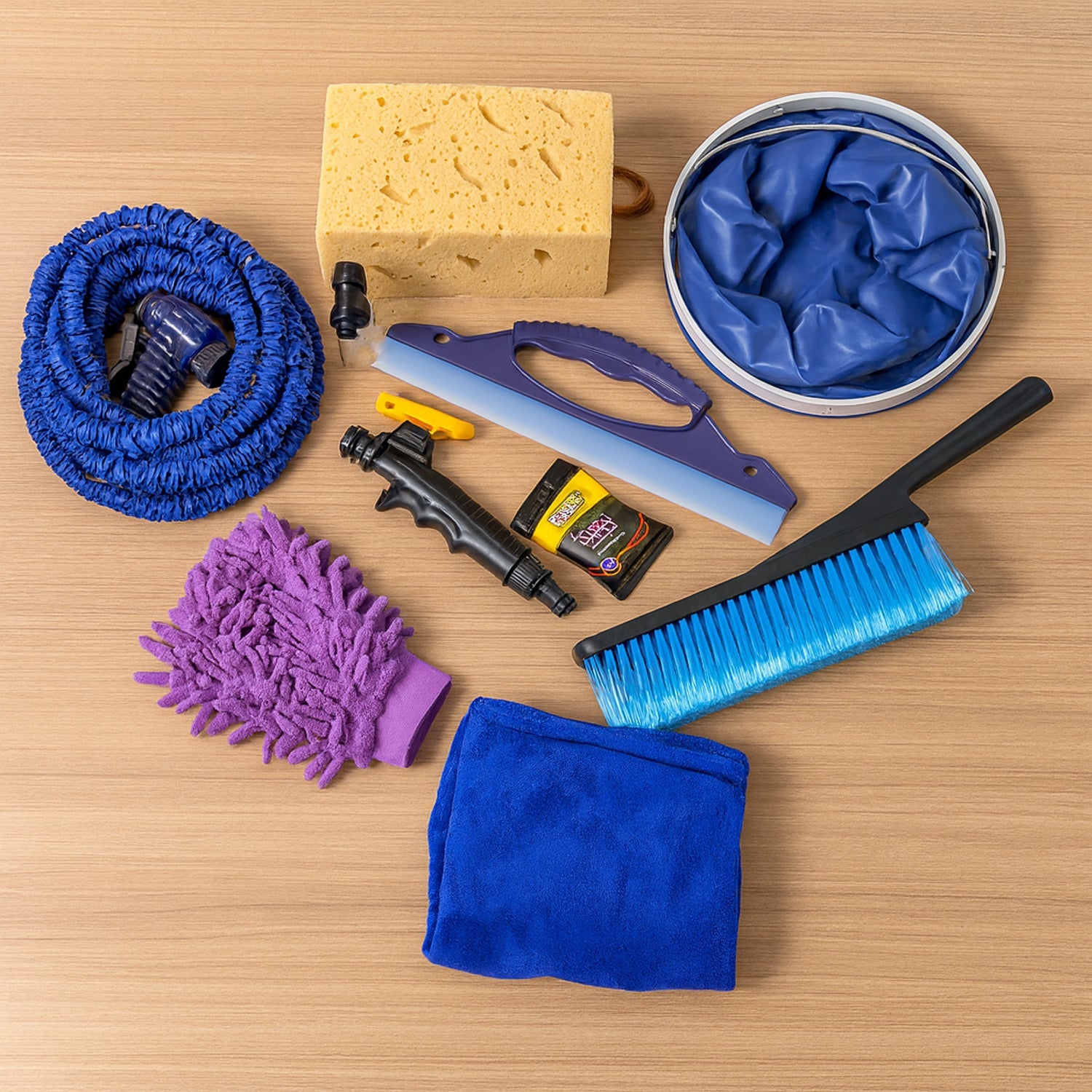 A car washing kit with a blue hose, purple mitt, yellow sponge, blue bucket, and various tools on a light wooden table.