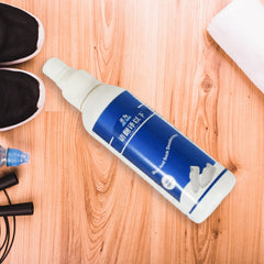 A white and blue bottle of shoe and sock deodorant lies on a light wooden surface next to black athletic shoes, a white